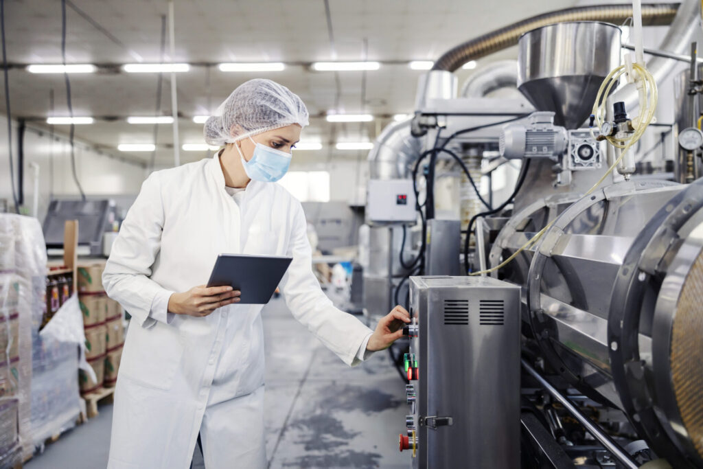 A female milk plant operator holding tablet and adjusting milk processing machine.