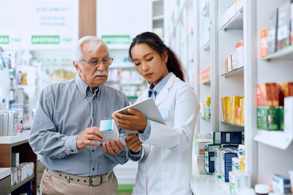 A pharmacist reviews drug information with a patient inside of a pharmacy.