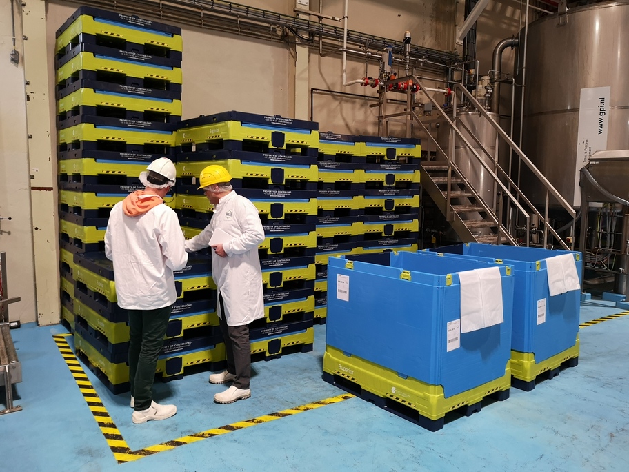 Inside a manufacturing facility, workers inspect neatly stacked Tosca Superior Hybrid bulk bins, while two Superior Hybrid containers stand unfolded and ready for use.