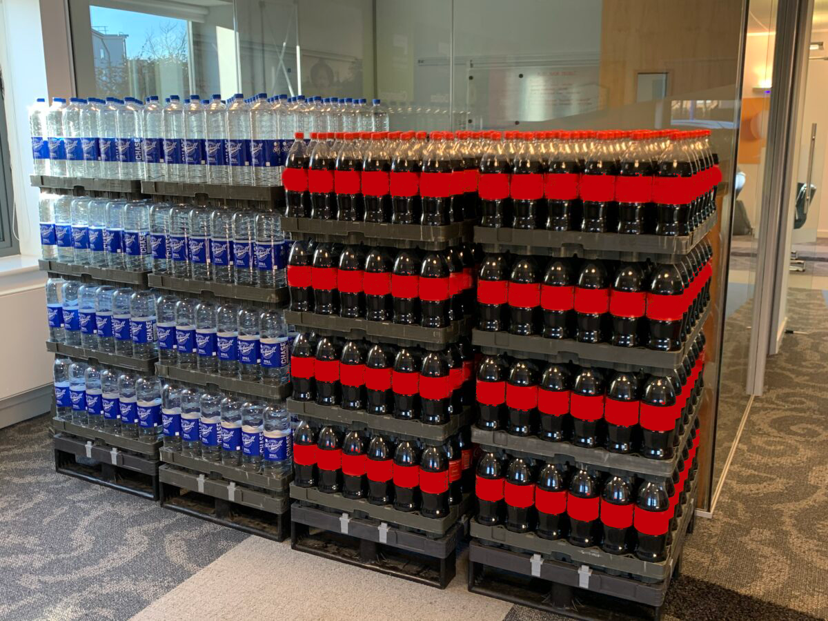 A Tosca Crystal Clear Crate displays assorted beverages in a grocery store. These standalone displays feature open-front crates for easy product access and are branded with signage on the top, sides, and bottom.