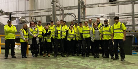 Service center employees take a group photo while wearing fluorescent yellow security vests. Employee mental health and safety are top priorities at Tosca.