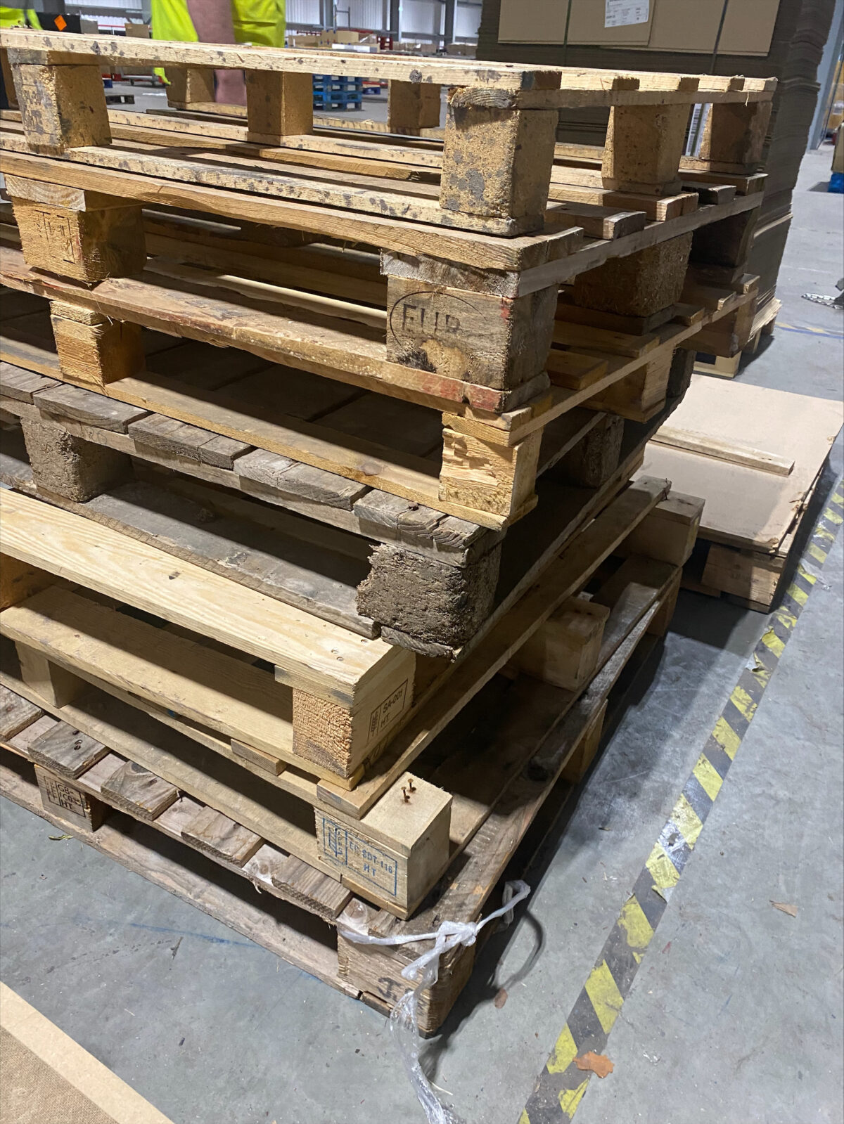 A stack of wooden pallets with raised nails, fragile boards, disproportionate sizes, and bulging wooden slats.