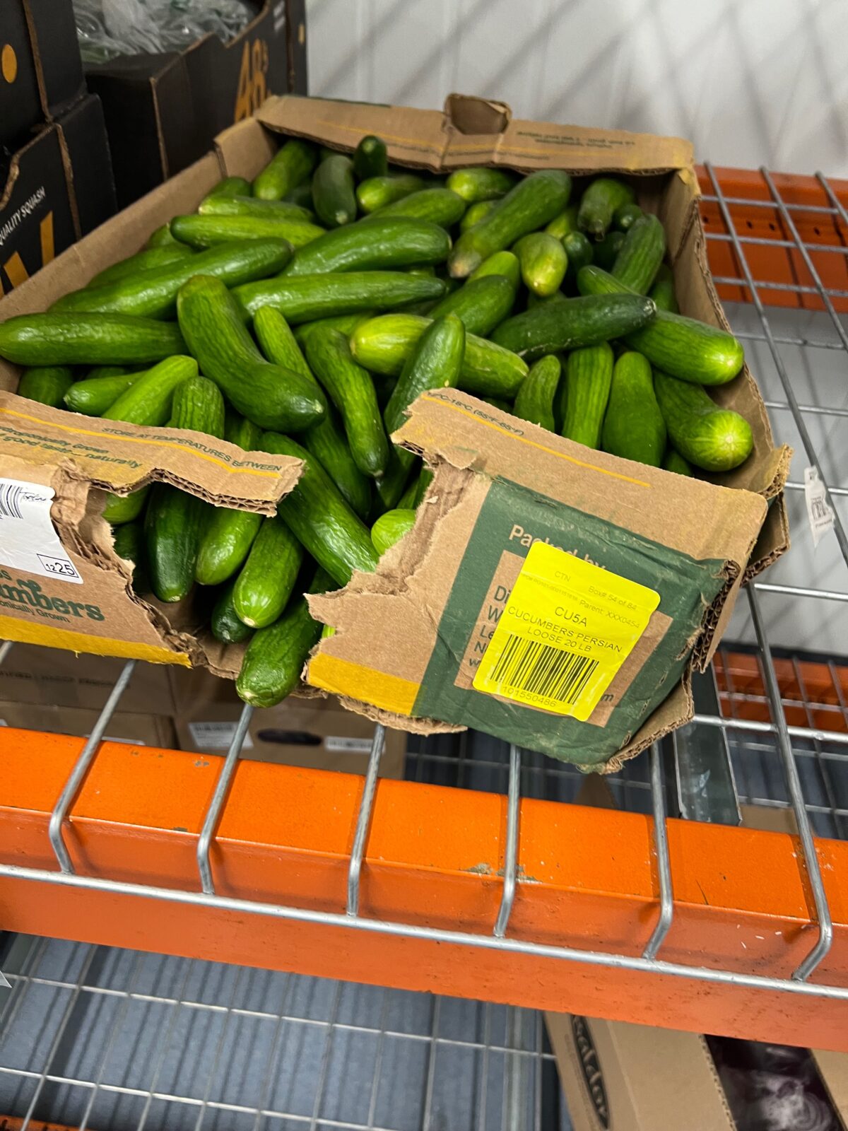 Cucumbers are falling out of a ripped side of a damaged corrugated cardboard box.