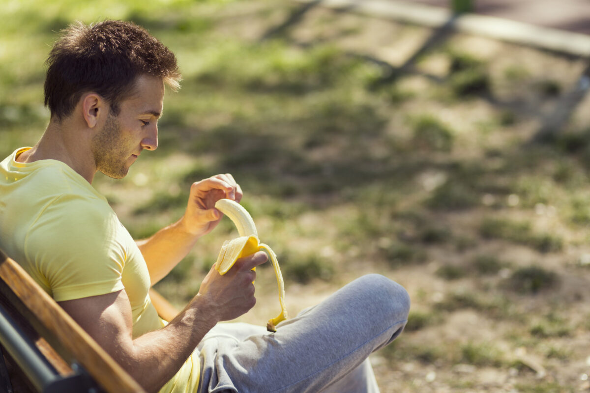 A man relaxes on a bench outside while enjoying a banana.