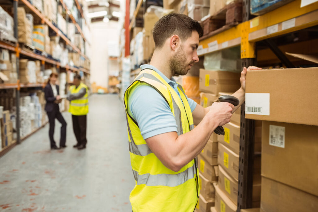 Warehouse worker scanning barcode on box in a large warehouse.