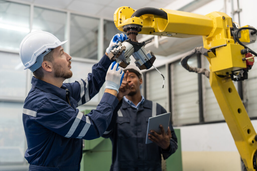 Two technicians inspect a robotic arm to ensure compliance with optimal functionality and safety.