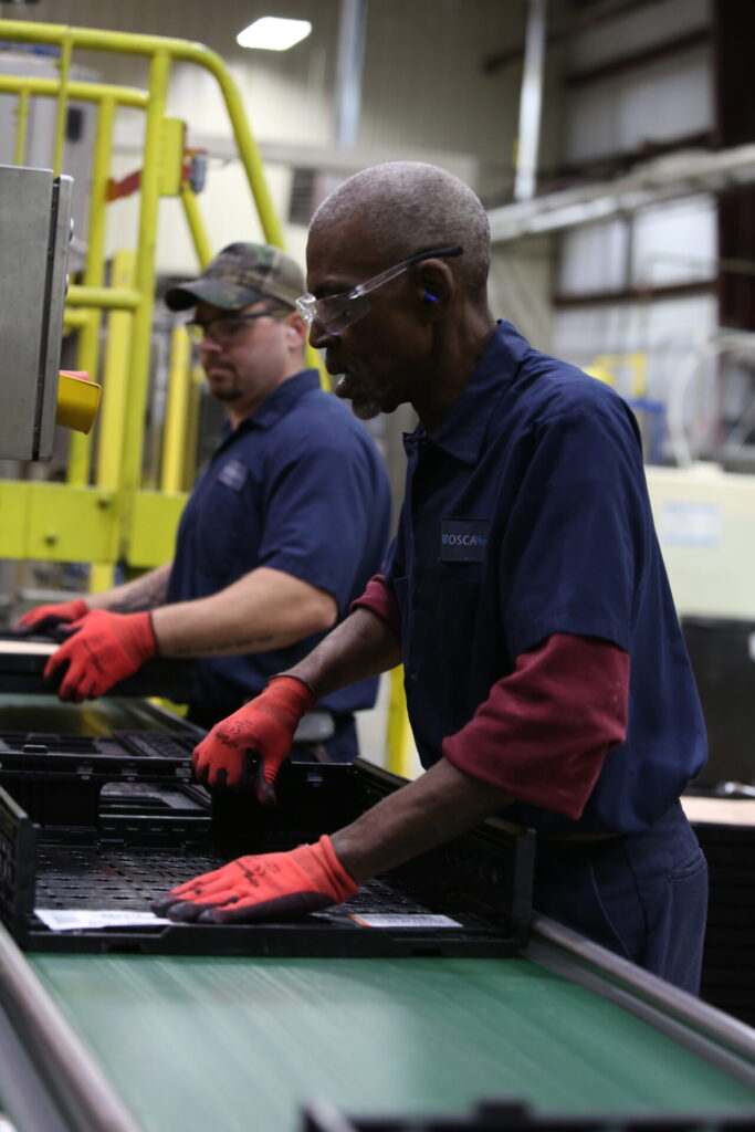 two men putting folded reusable crates on a machine