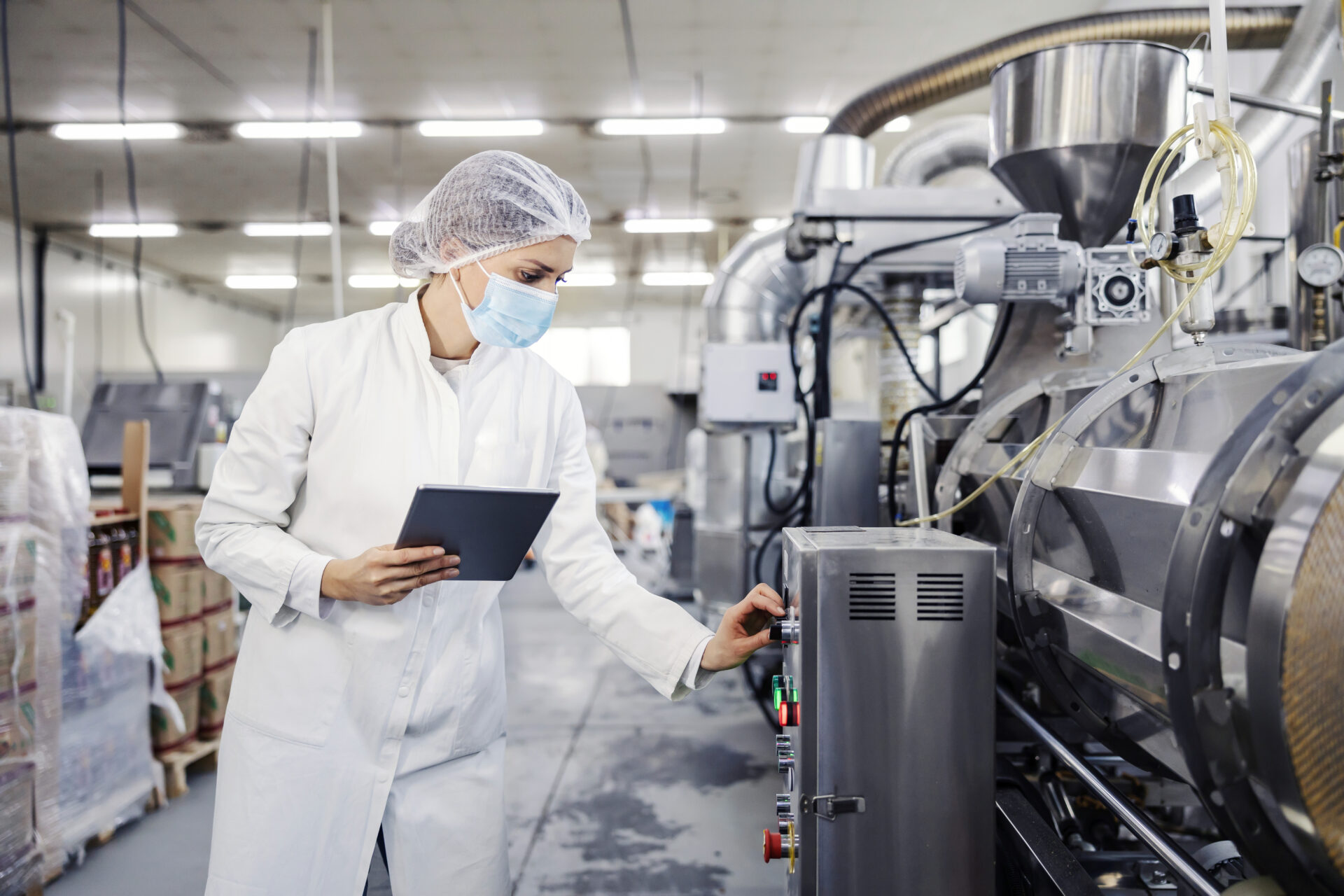 A female milk plant operator holding tablet and adjusting milk processing machine during corona virus.