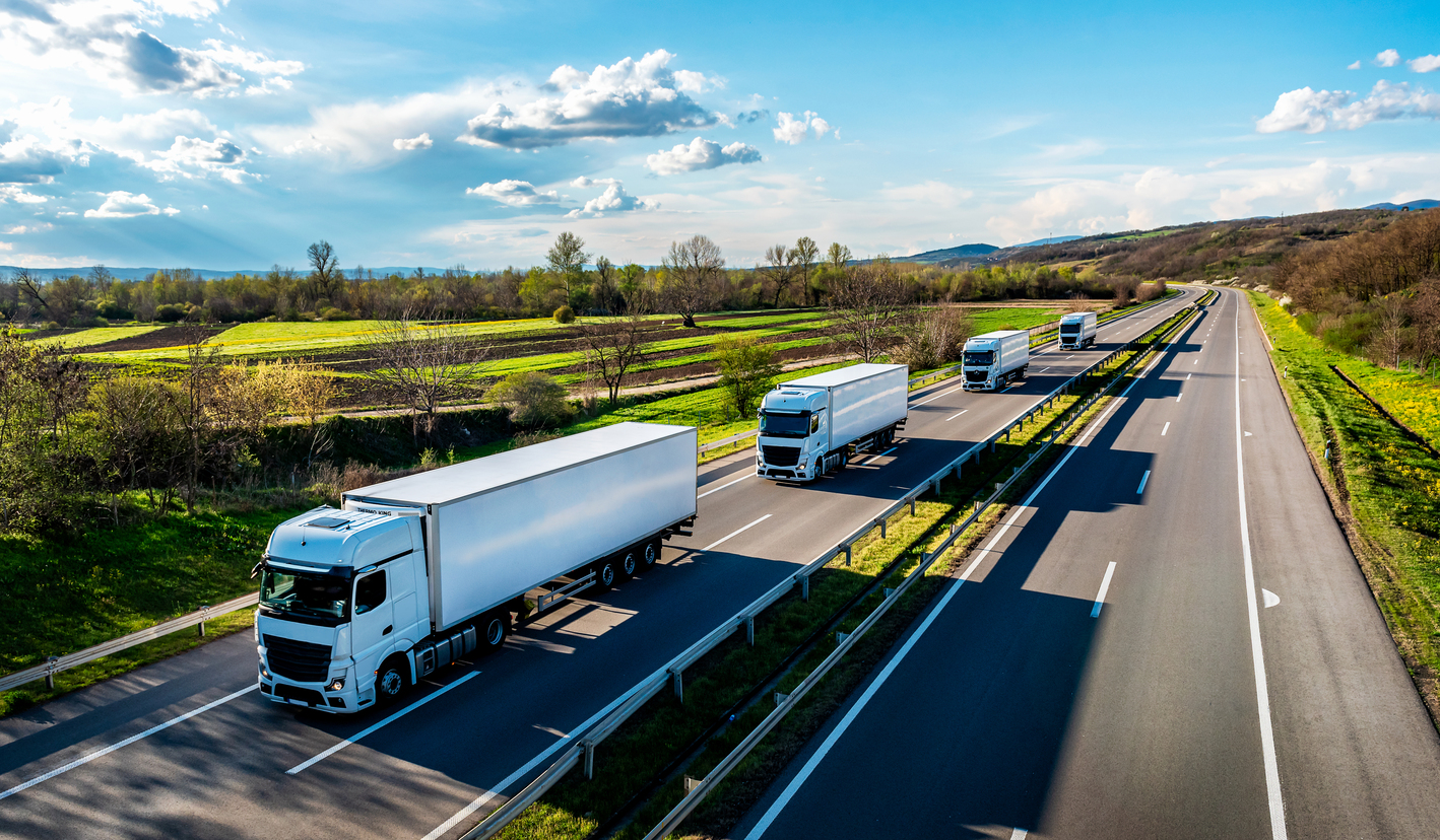 A fleet of trucks drive on a divided highway.